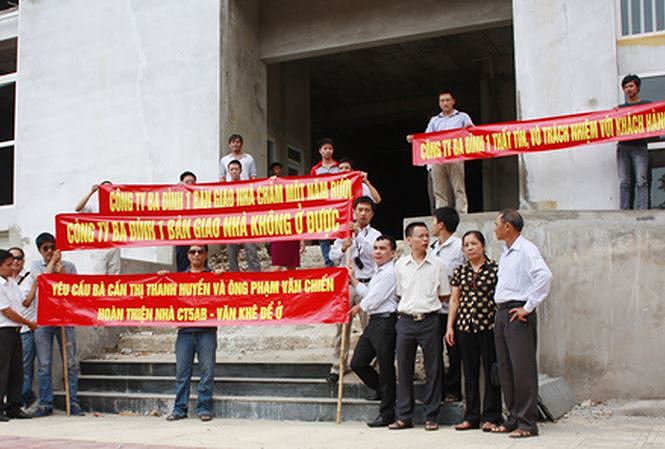 Dưới chân tòa nhà chung cư chưa hoàn thiện, một nhóm người đứng giơ băng rôn yêu cầu bàn hoàn thiện bàn giao nhà chung cư chậm tiến độ