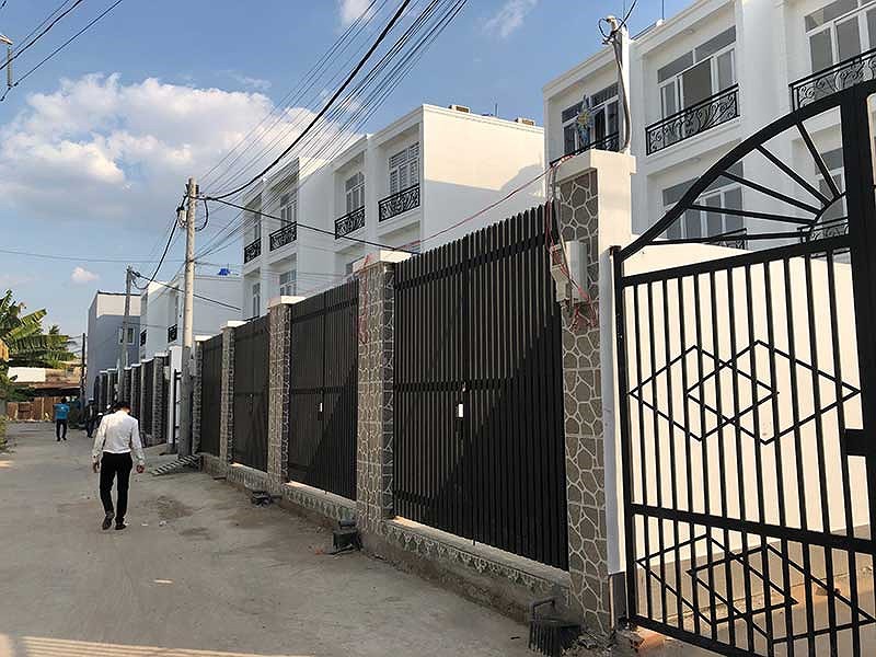 Ảnh chụp một dãy nhà xây san sát, phía trước là các cánh cổng sơn đen giống nhau đang khóa trái, bên ngoài là đường đi có một vài người đang qua lại nhà chung giấy