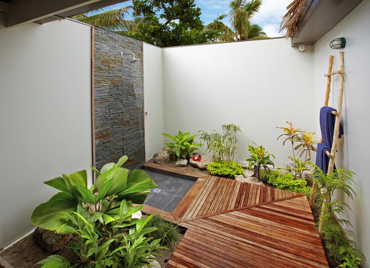 Phòng tắm ngoài trời tận dụng mảng tường và khoảng sân sau nhà gồm lối đi lát gỗ và tường ốp gạch nổi, kết hợp nhiều cây xanh Phòng tắm ngoài trời tận dụng mảng tường và khoảng sân sau nhà