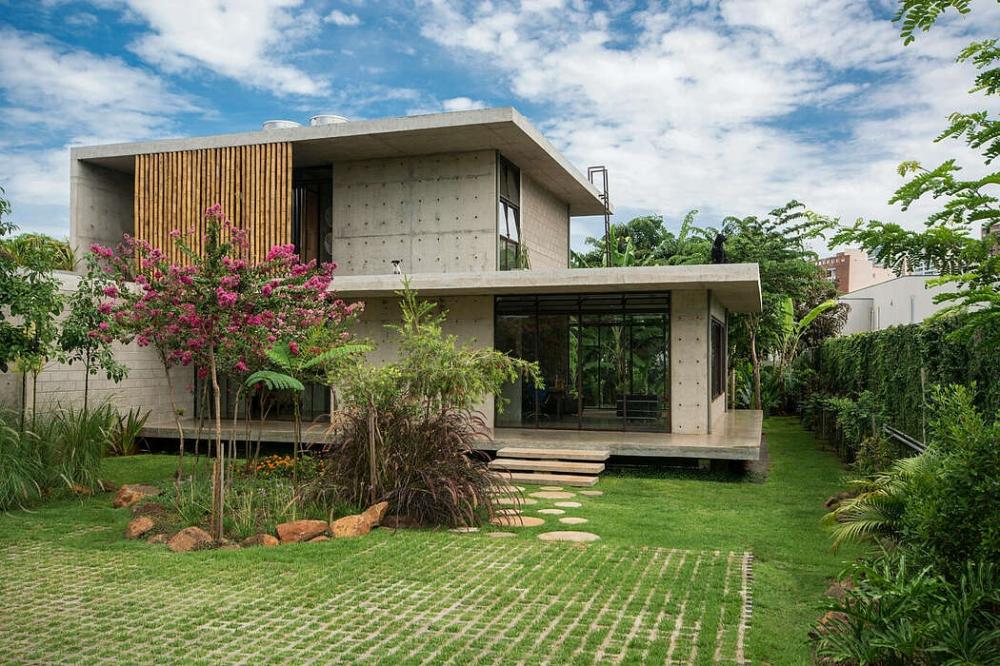 Ngôi nhà bê tông nằm giữa sân cỏ và khu vườn nhiều cây cối, giúp không gian thoáng mát hơn nhà bê tông