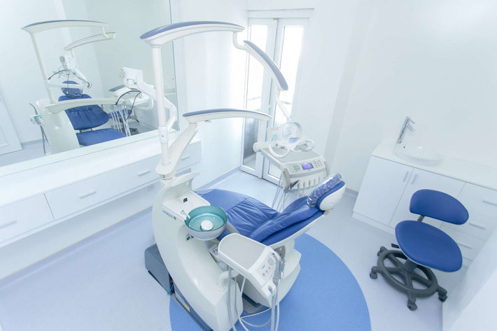Phòng khám răng màu trắng, ở giữa là máy điều trị, ghế nằm cho bênh nhân trang trí phòng khám răng