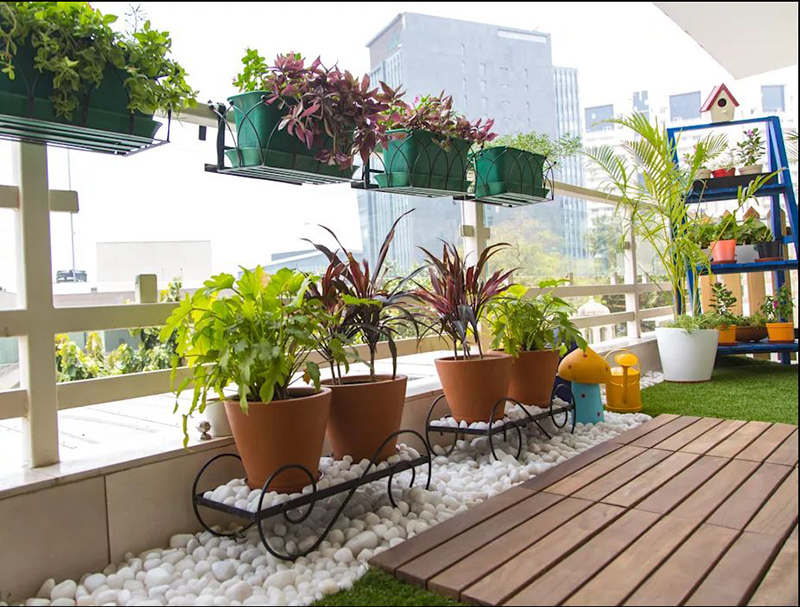 Nên chọn một vài phụ kiện trang trí để làm đẹp ban công. Ban công có các chậu cây treo trên lan can, bên dưới là kệ sắt để cây trên lớp sỏi trắng, sàn gỗ.