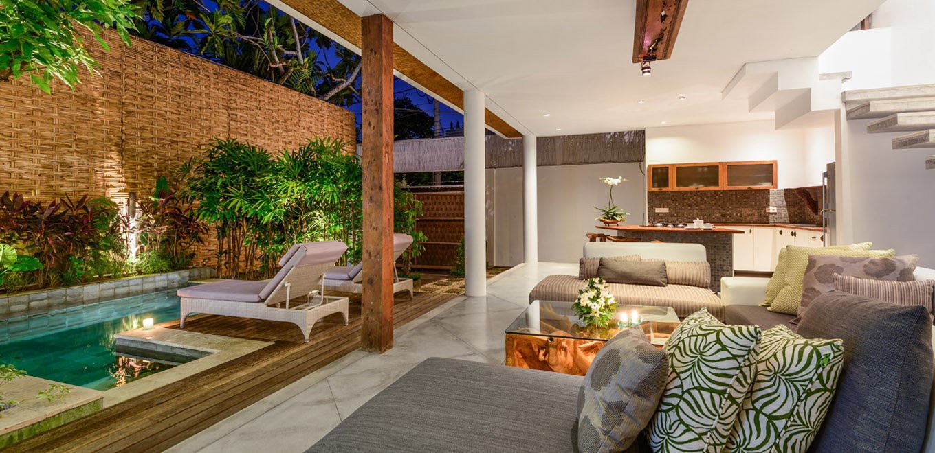 Phòng khách với nhiều sofa, gối ôm, đặt cạnh khung cửa kính lớn nhìn ra bể bơi phía trước biệt thự phòng khách đẹp