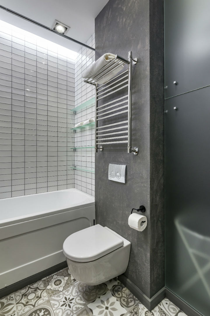 Toilet kiểu dáng hiện đại trong phòng tắm. Toilet màu trắng cạnh bồn tắm, bức tường bê tông xám và tường ốp gạch trắng.