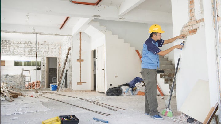Sửa nhà cuối năm cần chọn được đơn vị thi công uy tín. Nam công nhân đội mũ bảo hộ đang thi công bên trong một căn hộ màu trắng,