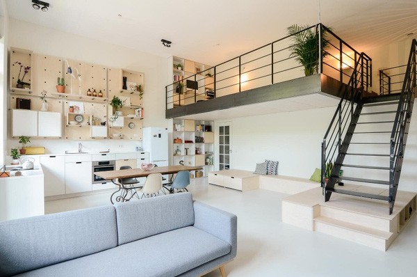 Sửa nhà cuối năm cần lên danh sách các đầu việc cụ thể. Phòng khách sau khi sửa nhà với sofa màu ghi, bức tường treo nhiều kệ, thang gỗ dẫn lên gác xép.