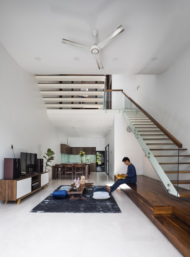 Thiết kế mở tạo cảm giác thông thoáng. Người đàn ông ngồi đọc sách trên bục gỗ ở phòng khách, dưới chân cầu thang, bên trong là bàn ăn, khu bếp.