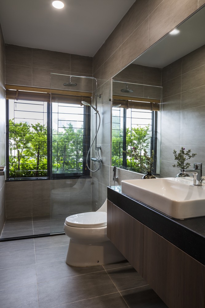Phòng tắm ốp gỗ màu tối sạch sẽ, có cửa sổ mở ra vườn, gương ​lớn gắn trên tường